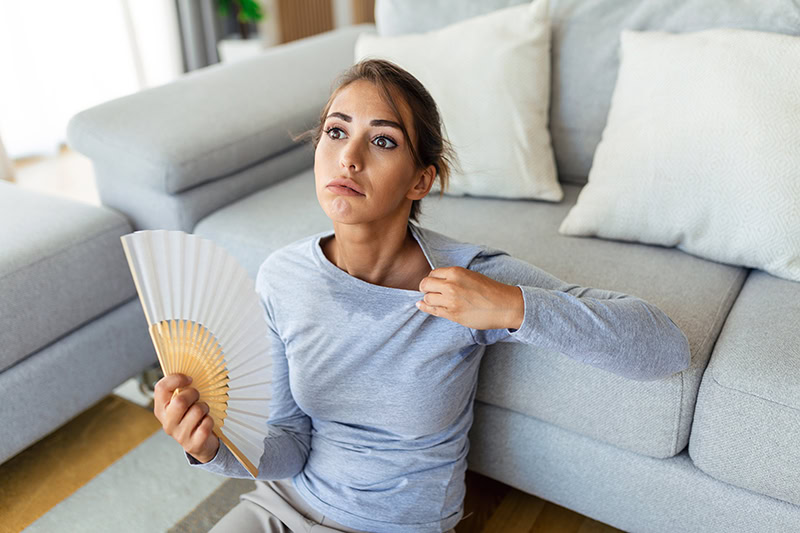 Stressed annoyed woman using waving fan suffer from overheating, summer heat health hormone problem, woman sweat feel uncomfortable hot in summer weather problem without air conditioner.
