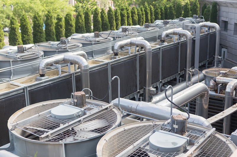 Commercial heat pumps on the top of a building with some green trees in the background