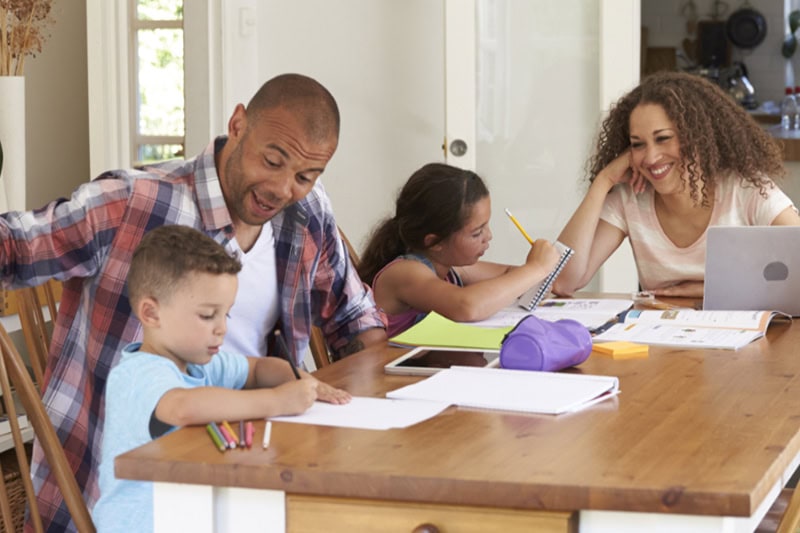 Young family with 2 kids sitting around the dining room table, while the kids do homework.